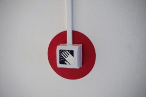 A fire alarm system's hand panel mounted on a wall is surrounded by a red circle to help it stand out.